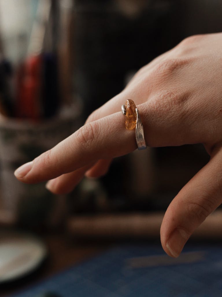 Close-up of a hand adorned with a silver ring featuring a gem, in a softly focused artistic indoor setting.