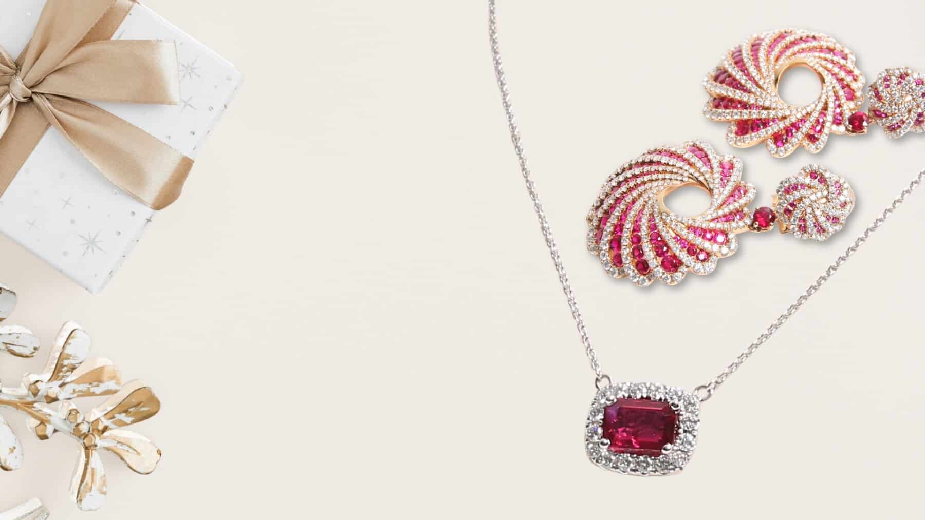 Ruby and diamond necklace and matching swirl earrings set, placed next to a holiday gift box for the Harry Glinberg Signature Gift Guide.