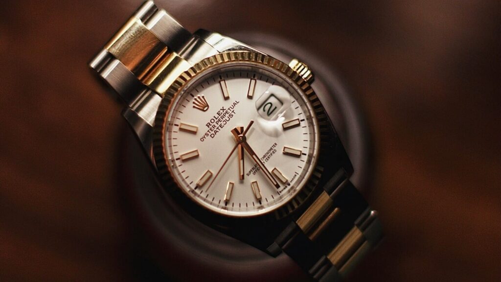 A two-tone Rolex Datejust with a fluted bezel resting on a dark wood surface.