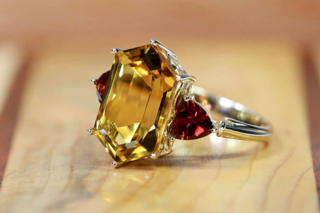 An emerald-cut yellow citrine center stone ring with trillion-cut red garnet side stones on a wooden background.