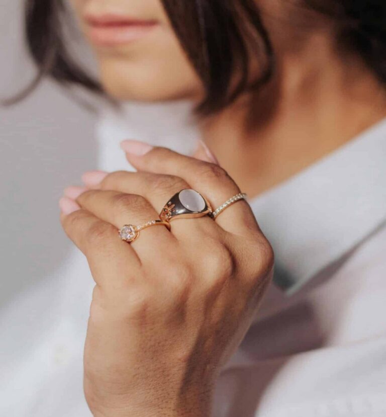 Woman wearing a stack of luxury gold fashion rings and a gold chain bracelet from Harry Glinberg Jewelers